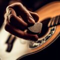 A guitarist's hand holding a pick, ready to strum, showcasing the best acoustic guitar picks for strumming